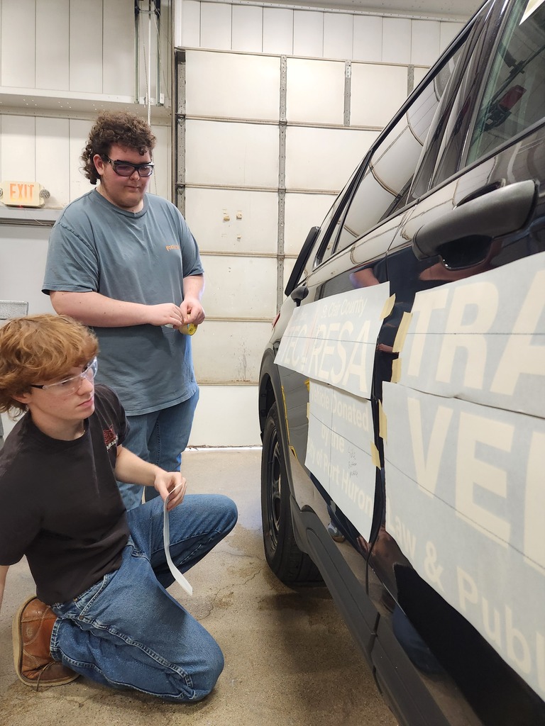 Two Collision Repair students apply decals to a black decommissioned police cruiser inside an automotive lab at St. Clair TEC.