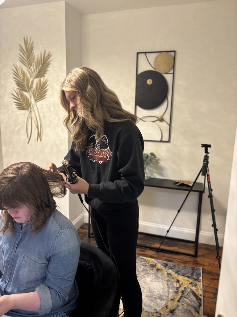 A TEC student curls another student's hair in a salon setting as part of the Prom Experience event.