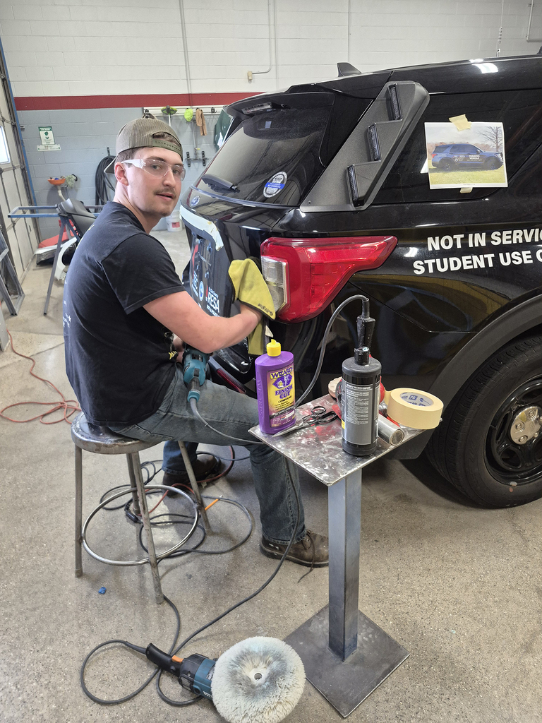 A Collision Repair student sits facing the tailgate of the Law & Public Safety vehicle as he uses a cloth to buff it out.