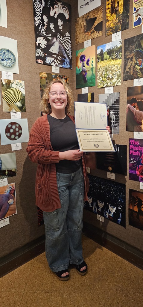 Aubrey Beier stands in front of the artwork display holding her certificate