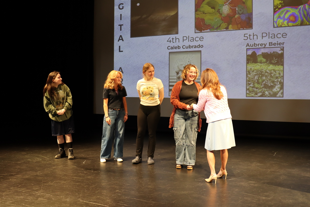 Aubrey Beier, standing on stage with other students, receives her award from Lisa McClain