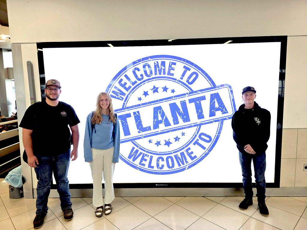 TEC students Michael Carrier, Rori Cowhy, and Blake Duvall stand in front of a digital screen that reads, "Welcome to Atlanta" inside the Atlanta, GA airport.