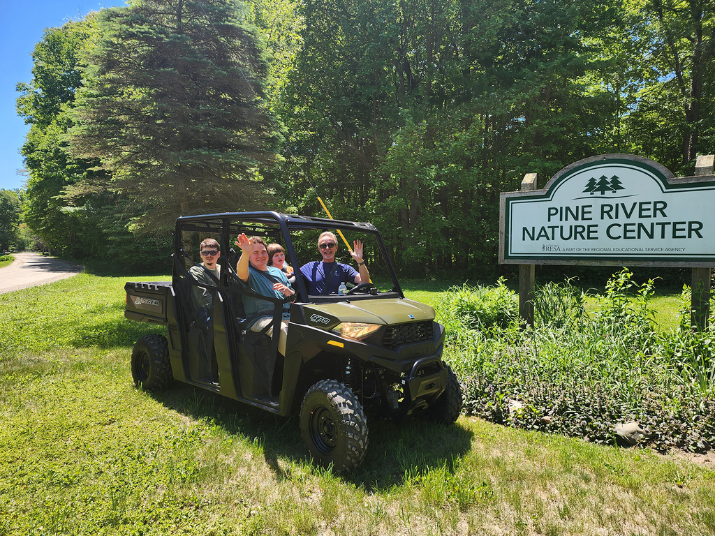 Woodland's Can-Do Crew sit in the new Polaris vehicle waving at the camera. The PRNC sign is visible in the background.
