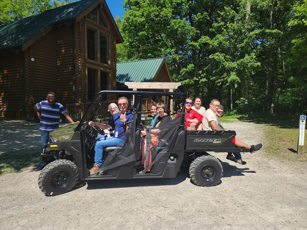 Woodland's Can-Do crew sit on the Polaris vehicle in front of the Pine River Nature Center lodge.