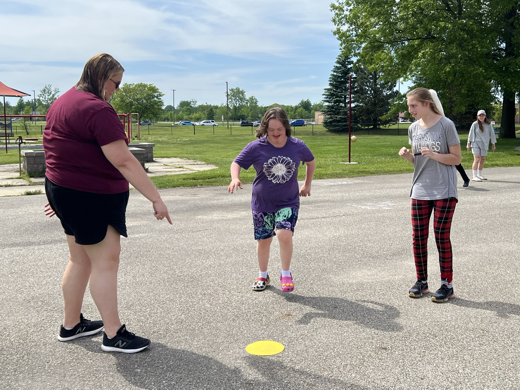 A smiling Woodland student runs toward a yellow dot on the ground that a staff member points at
