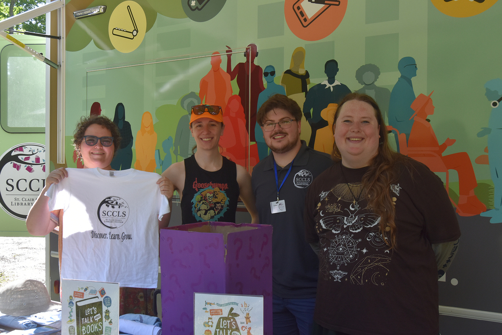 Four smiling St. Clair County Library staff members pose in front of the Bookmobile. 
