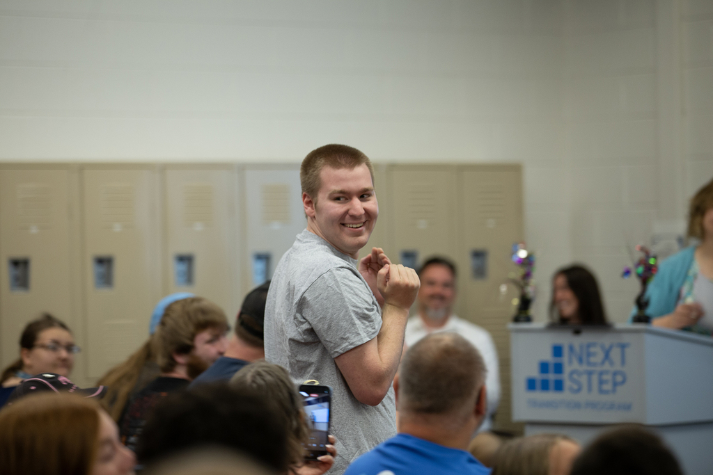 A Next Step student smiles at his family as he walks to accept his completion ceremony.