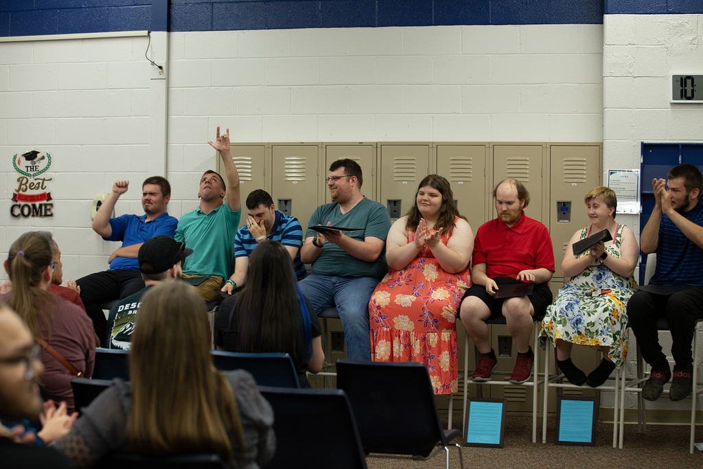 The Next Step completers sit in a row during the completion ceremony. Some with hands in the air, other clapping, and others wipe tears from their eyes.