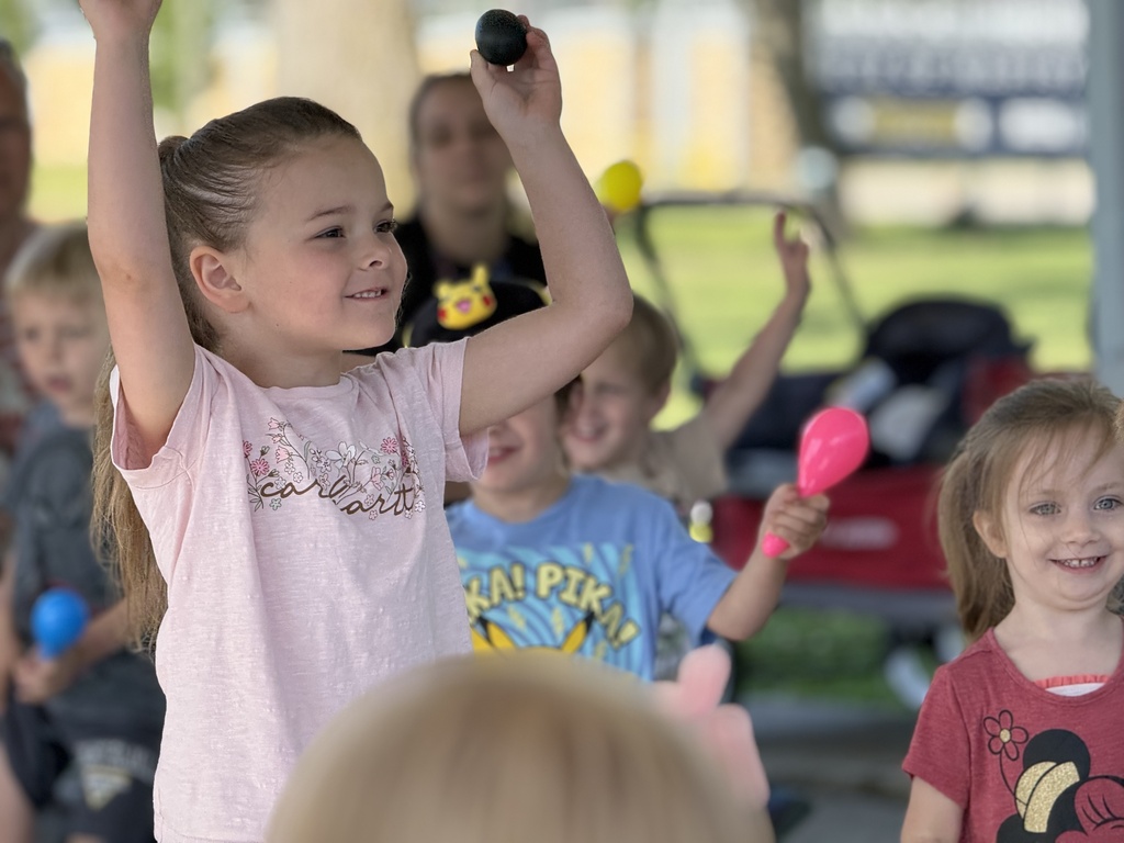 A young child holds noisemakers with their arms in the air