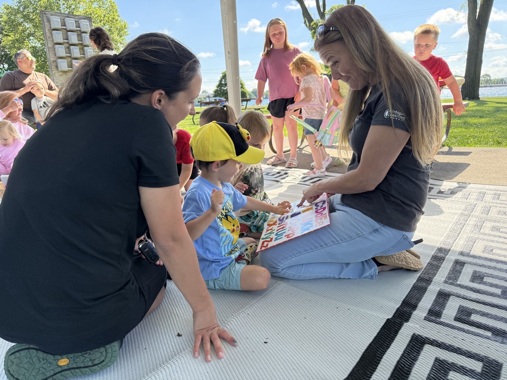 Tara from PBS holds a picture book in front of two children