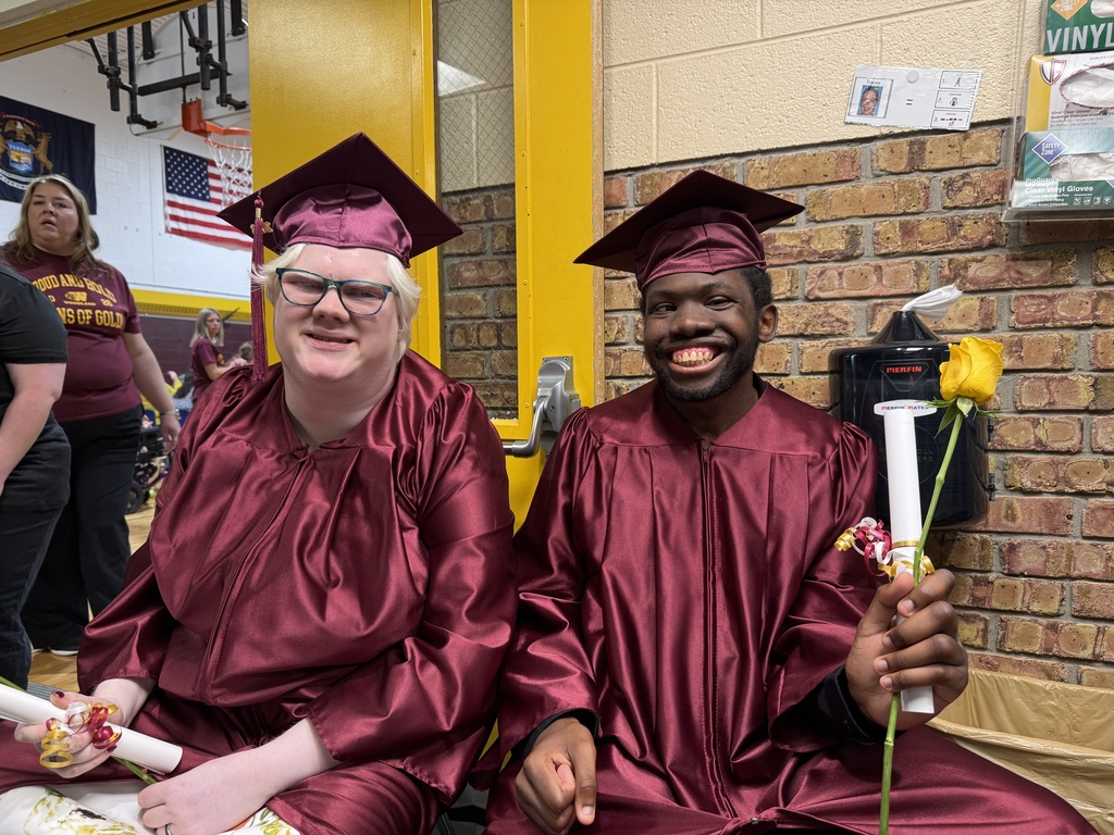 Smiling completers Camryn and Tyrique wearing graduation caps and gowns hold certificates 