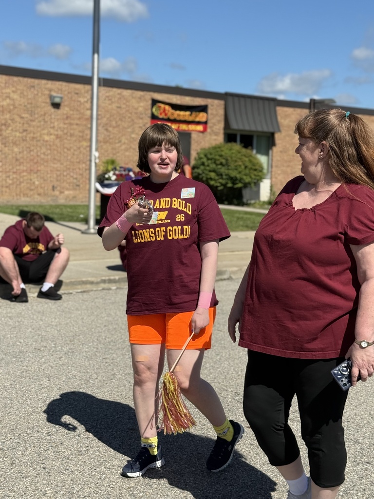 A Woodland student wearing a school shirt and holding a pom-pom walks outside with a family member during the completion parade