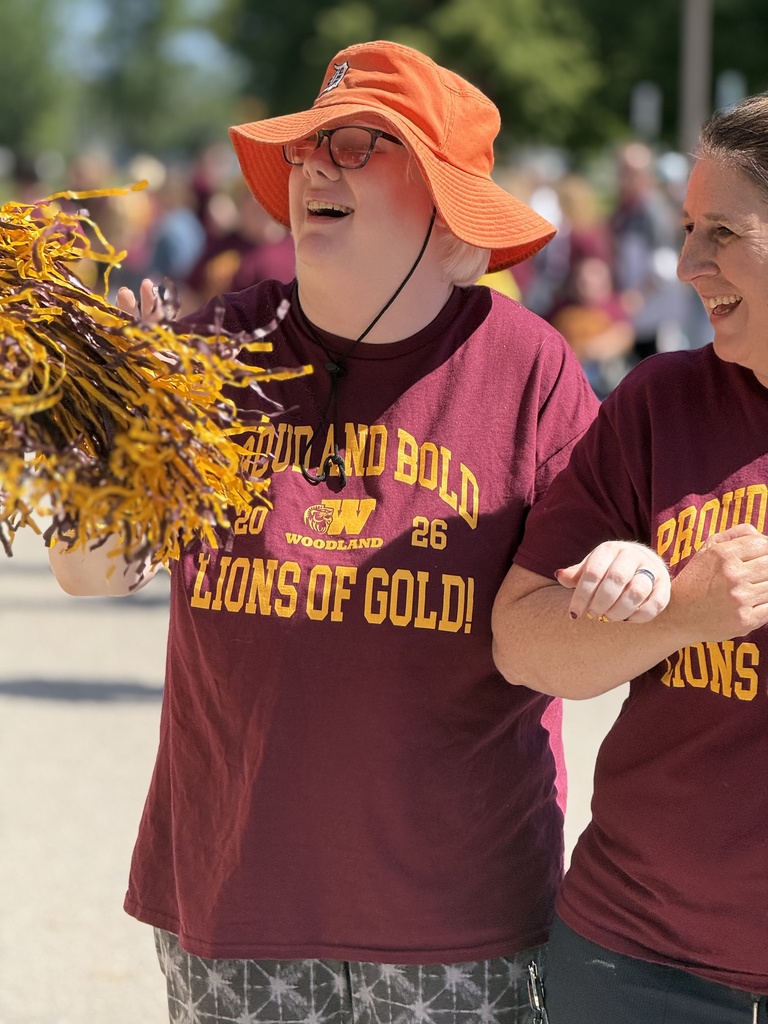 A Woodland completer holding a pom-pom walks arm-in-arm with a staff member in front of the school