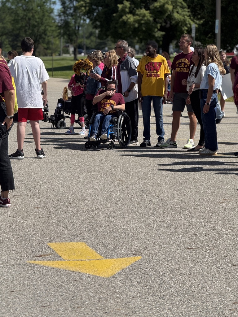 A Woodland completer wearing a school shirt sits in their wheelchair among staff and classmates in front of the school during the Completion parade
