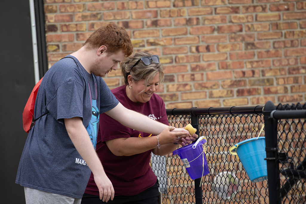 A Woodland staff member helps a student place an item into a bucket during the school's field day activities