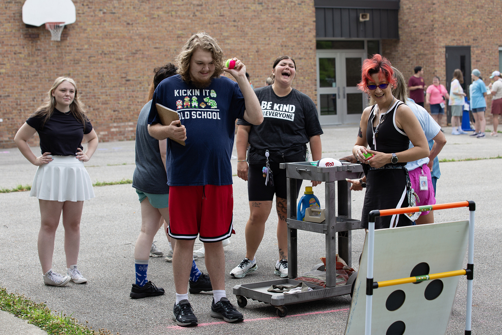 A Woodland student tosses a small into a ball toss game. Staff and student look on smiling.