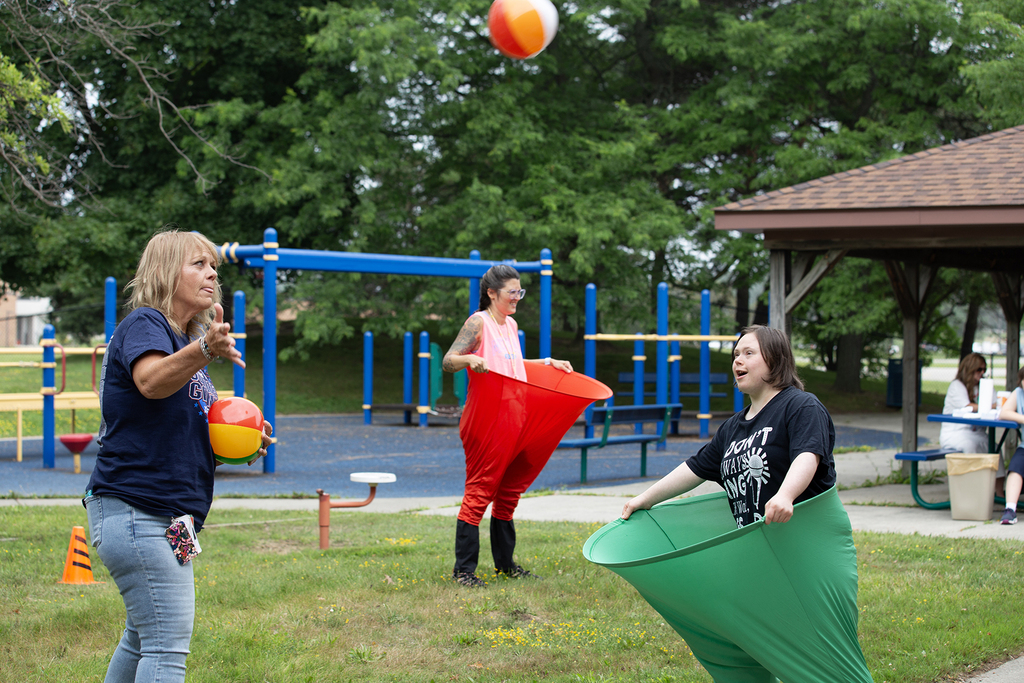 A Woodland student and staff member play a ball toss game. The student wears "pants" with a large hoop at the waist to try and catch the balls.