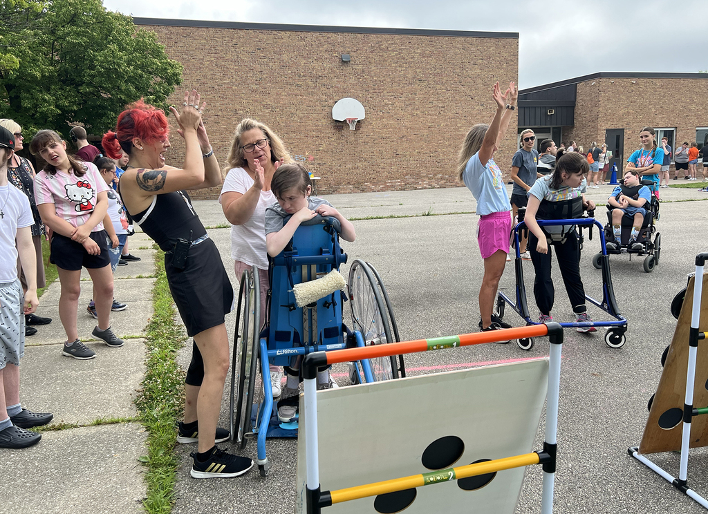 Woodland students in a standing wheelchair and walker play a ball toss game as staff clap and cheer them on during the school's Field Day