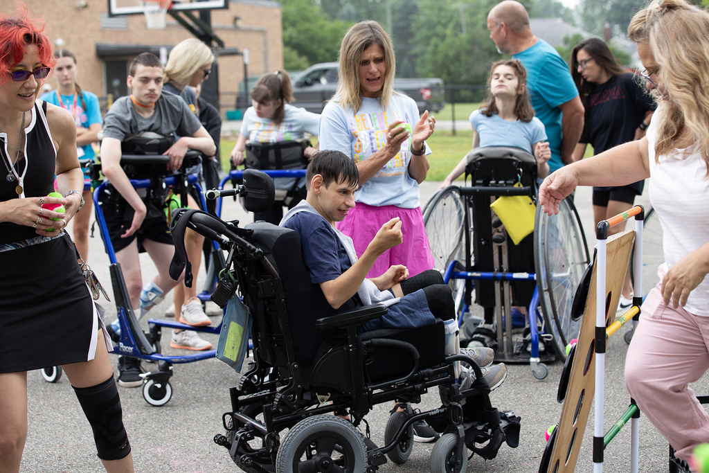 A Woodland student in a wheelchair plays a ball toss game during the school's field day. Staff and students cheer him on.