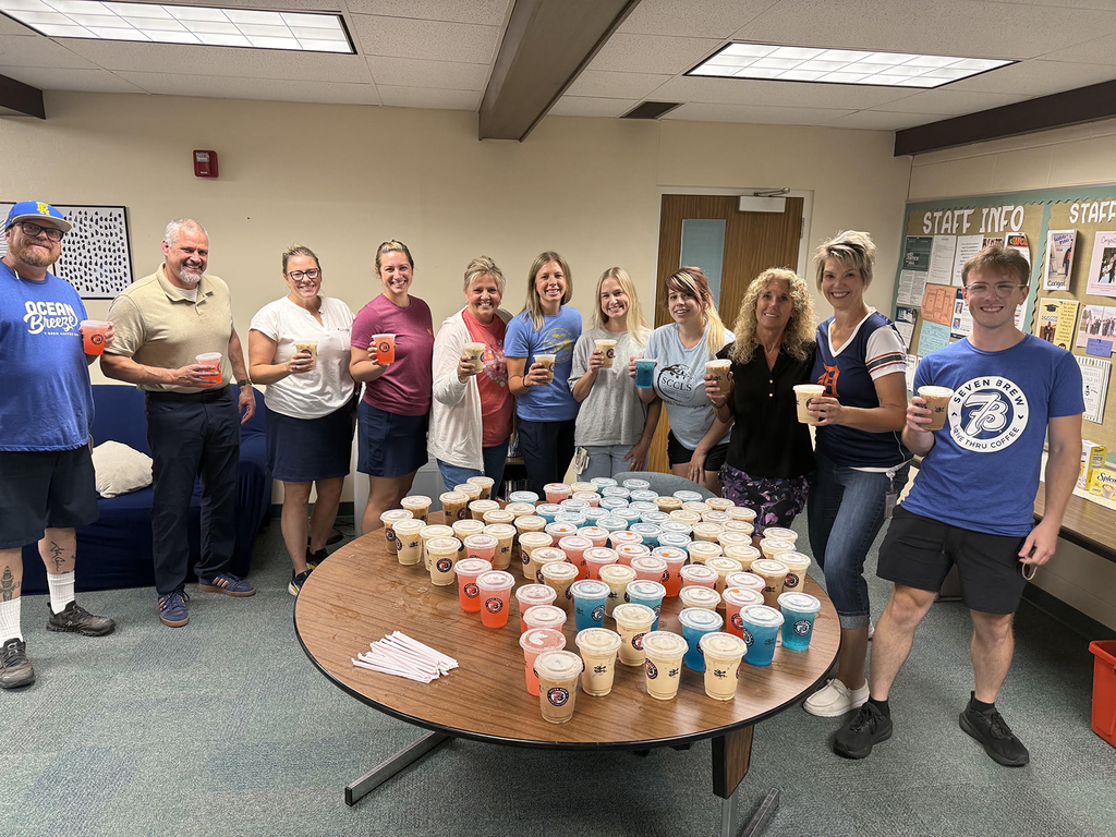 Woodland staff holding drink cups stand around a table full of coffee and energy drinks.