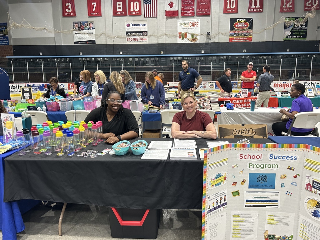 Ari McCoy and Jessica Malburg sit at a table with water bottles, stickers, and print resources at the Back-to-School Backpack Giveaway