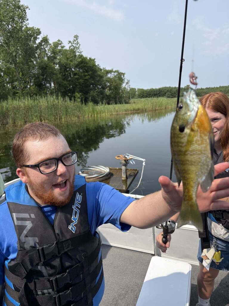 A smiling Woodland student reaches for a fish on a hook