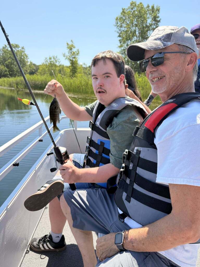 A Woodland student holds a fishing ord and in one hand and a fish in the other
