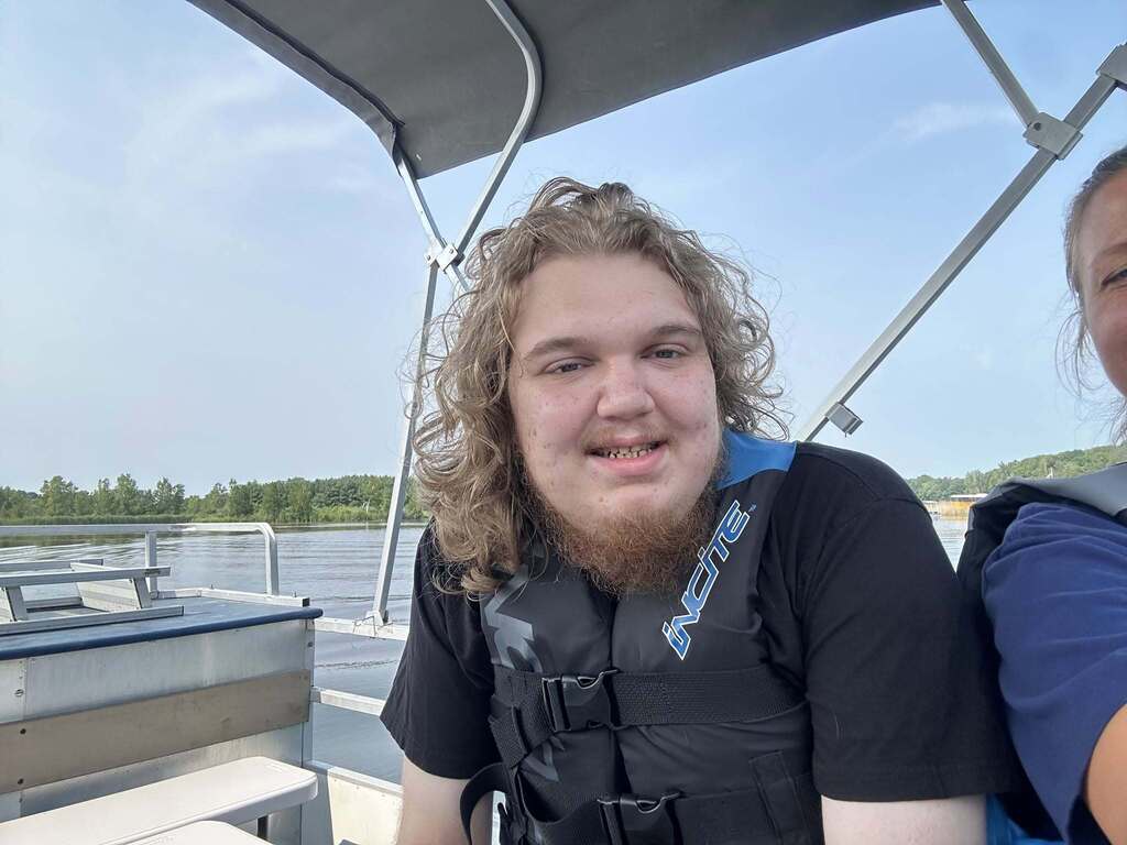 A smiling Woodland student wearing a life jacket sits on a boat