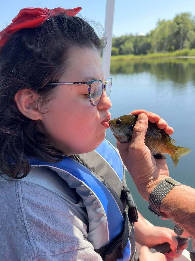 A Woodland student wearing glasses and a hair bow kisses a fish being held by an adult