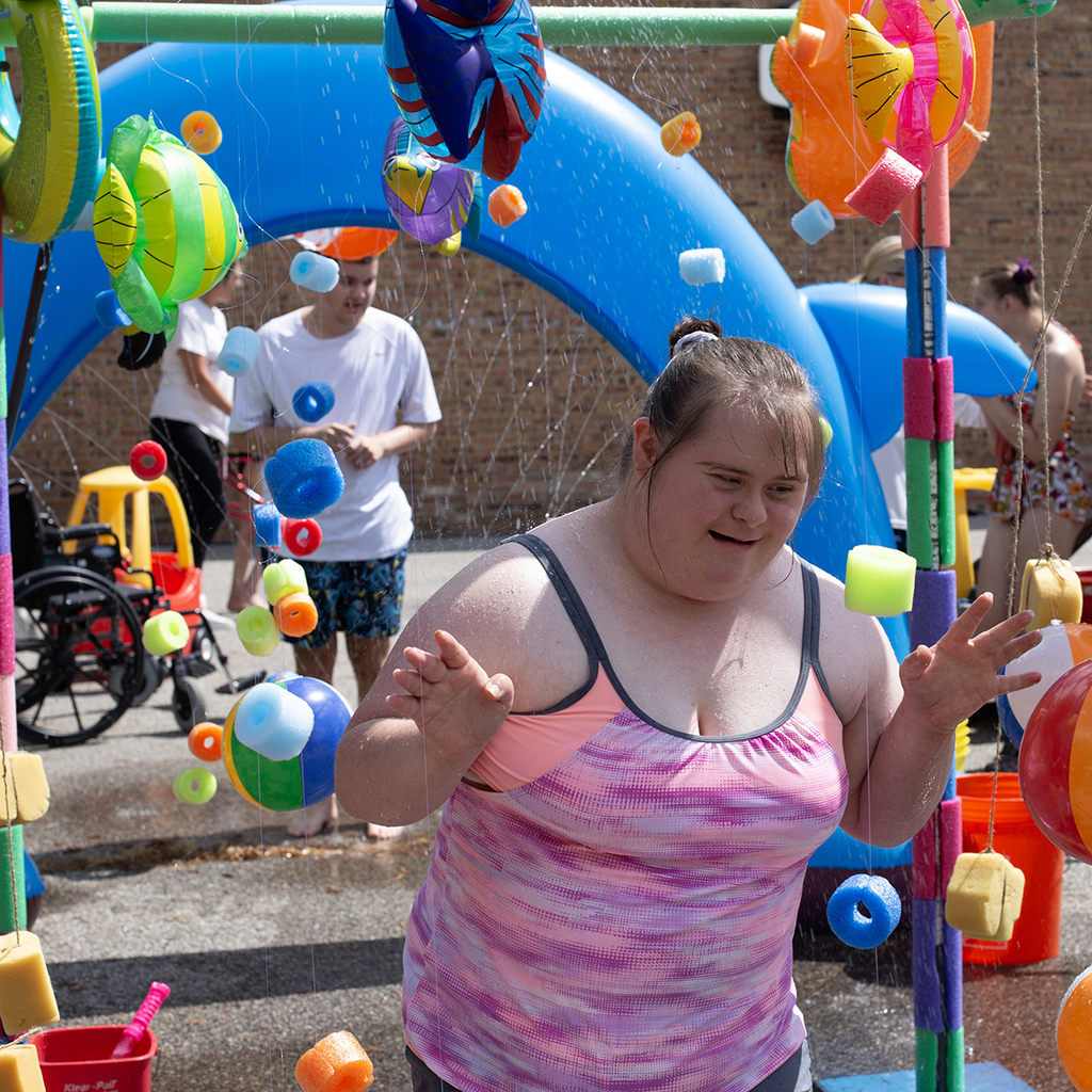 A smiling Woodland student walks under a colorful sprinkler feature