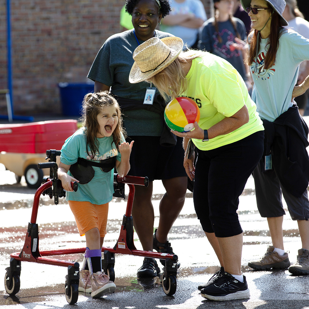 A Woodland student smiles wide as she walks through puddles. A staff member holding a beach ball stands close by.