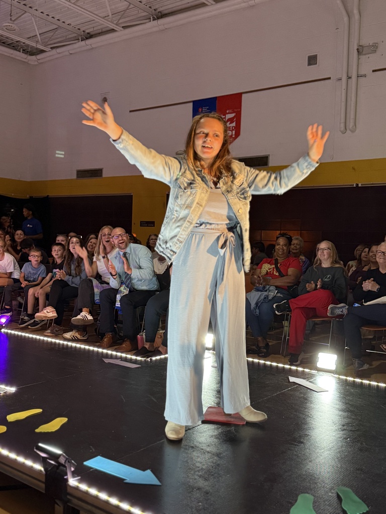 A Woodland student smiles with arms outstretched on a raised runway