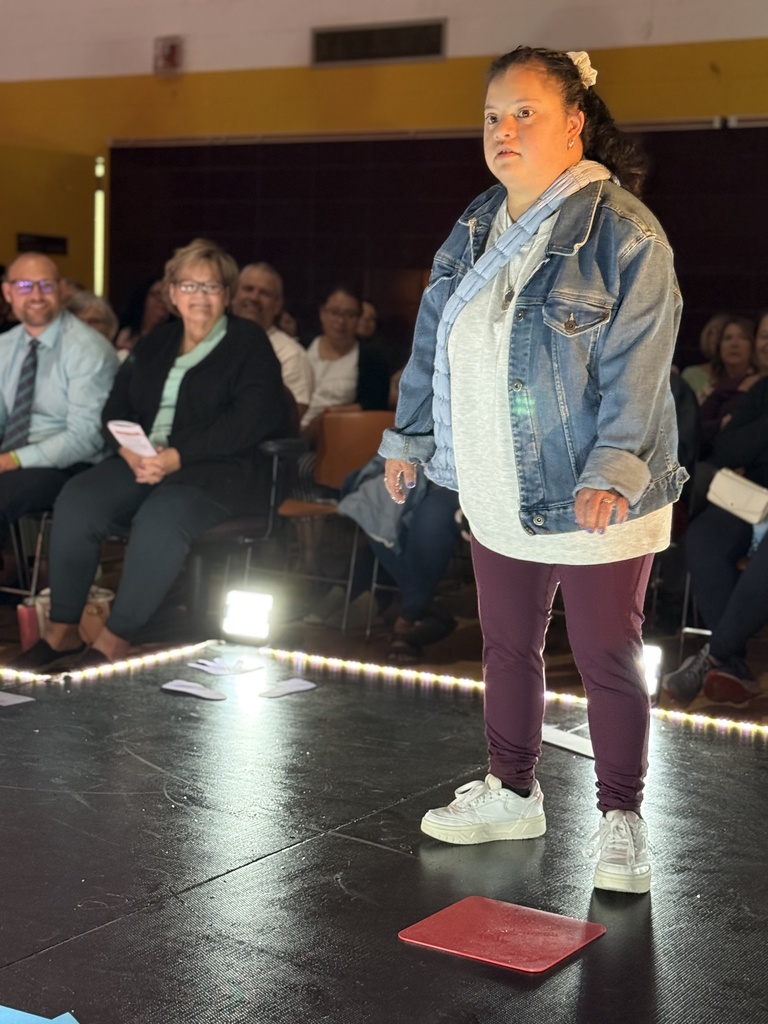 A Woodland student wearing purple leggings, a gray sweatshirt, and jean jacket poses at the end of a raised runway