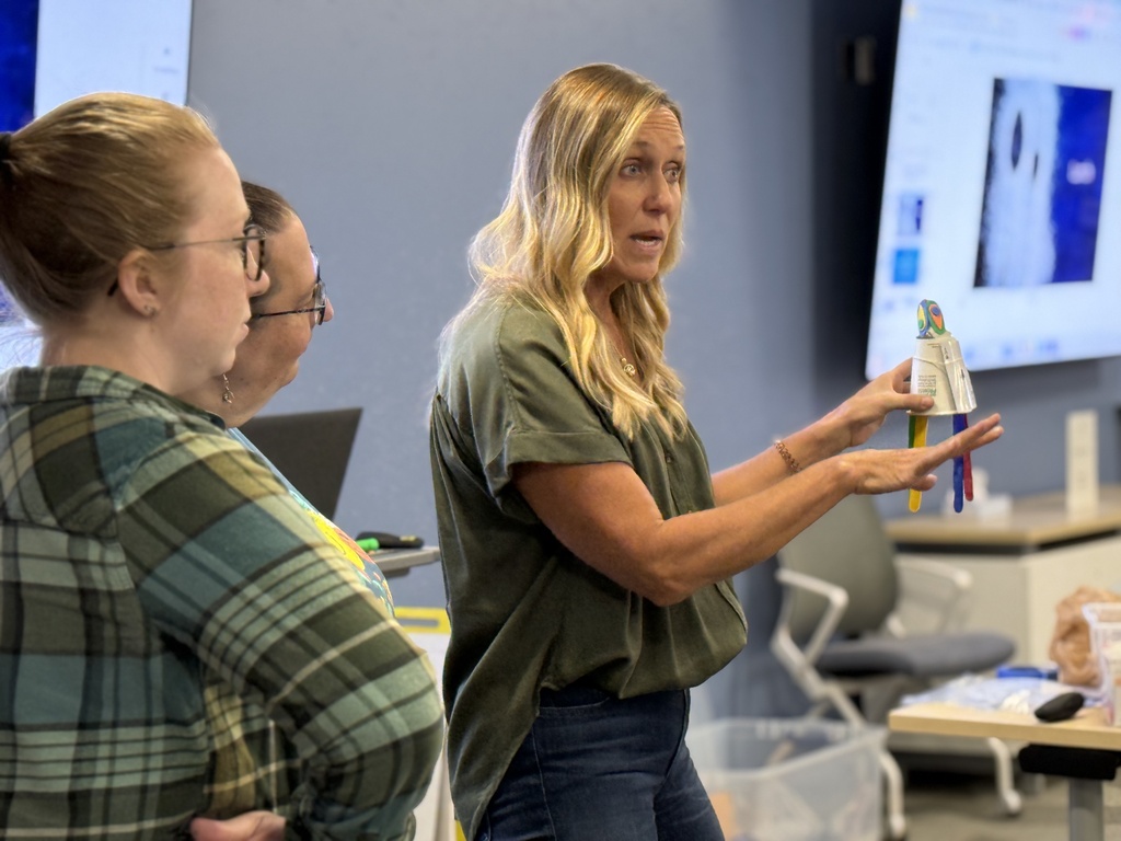 A 2nd Shift participant holds a hand-made object constructed of various art supplies while her two members look on