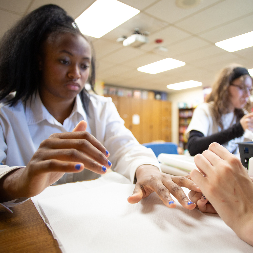 A Woodland holds her hand still as a Cos students paints her nails