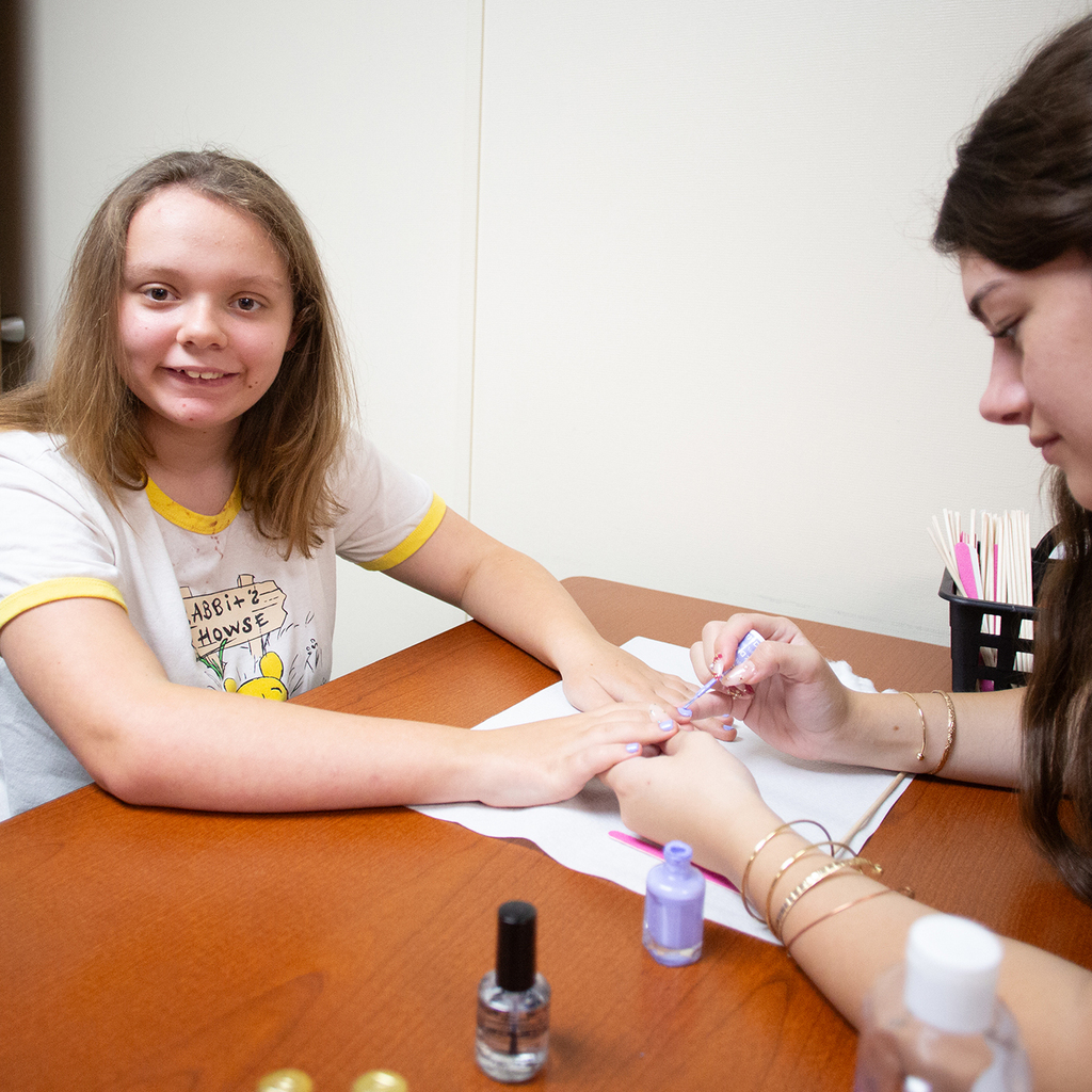 A Woodland student smiles at the camera as a Cos student paints her nails