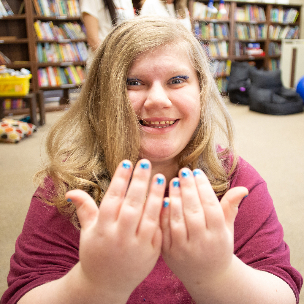 A smiling Woodland holds her hands up to the camera displaying her bright blue painted nails