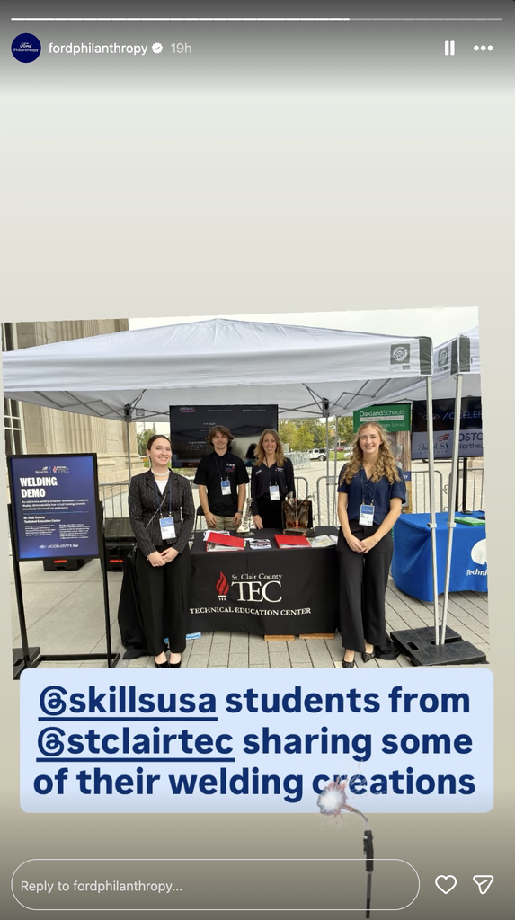 TEC staff and students stand under a canopy behind a table with the TEC logo on a tablecloth