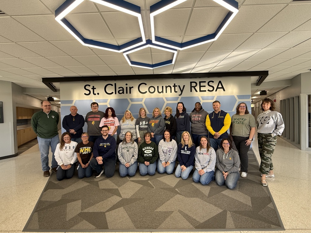 Admin Building staff pose wearing their favorite college gear. The "St Clair County RESA" sign is in the background