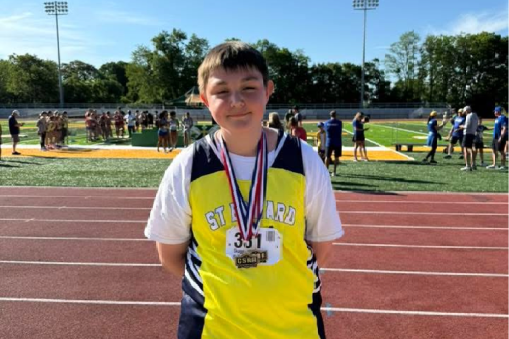 St. Edward student Matthew Skaggs stands on a track wearing his team uniform and medals after being named City Champion in both javelin and shot put.