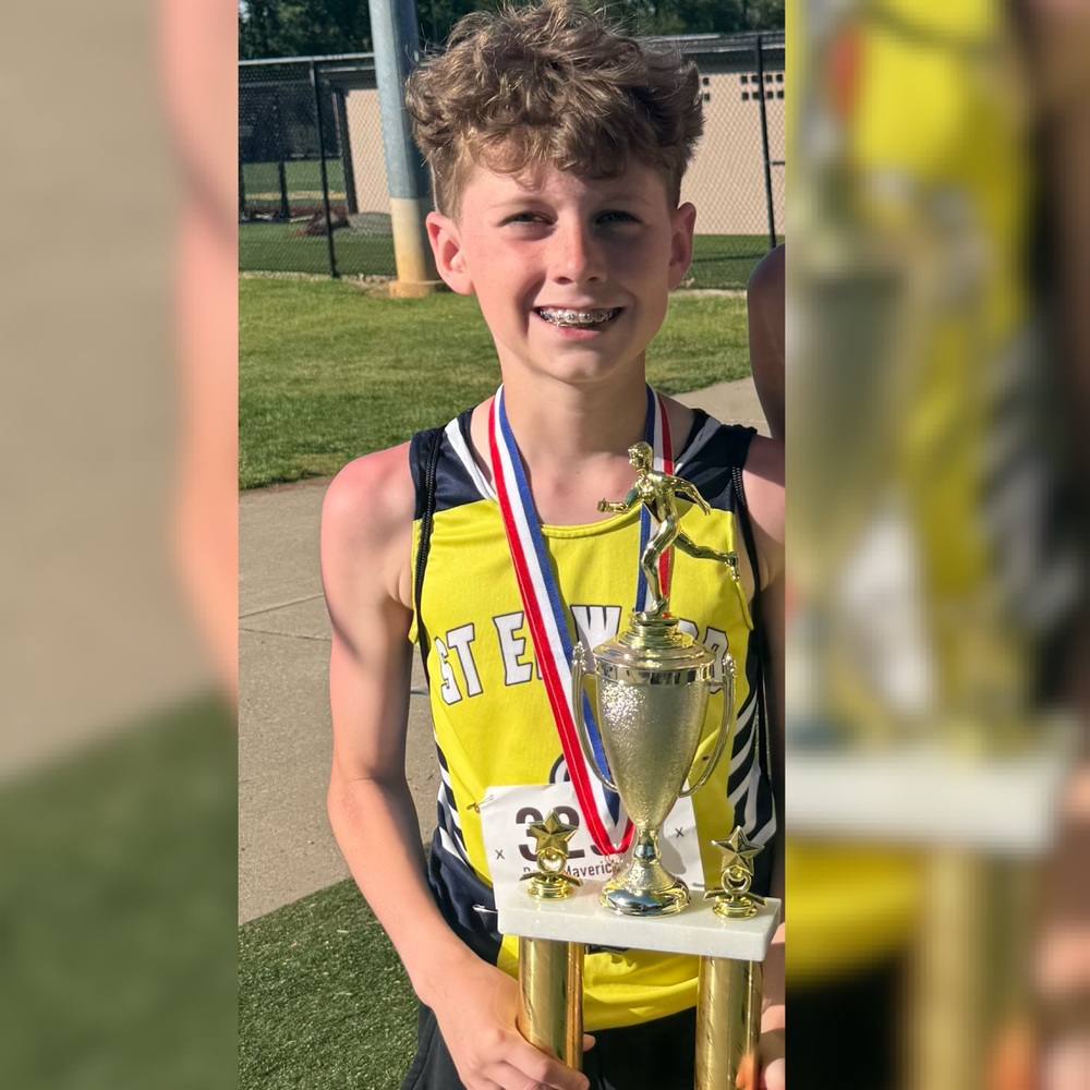 St. Edward student Maverick Potts smiles while wearing medals and holding a large city championship trophy after winning the 1600m at the Track and Field City Meet.