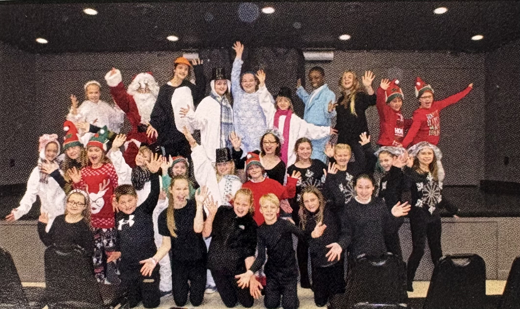 Throwback to Ade Goring at  St. Edward Drama Club. He is in the blue coat with the cast posing together on stage after a performance, celebrating student talent and creativity.