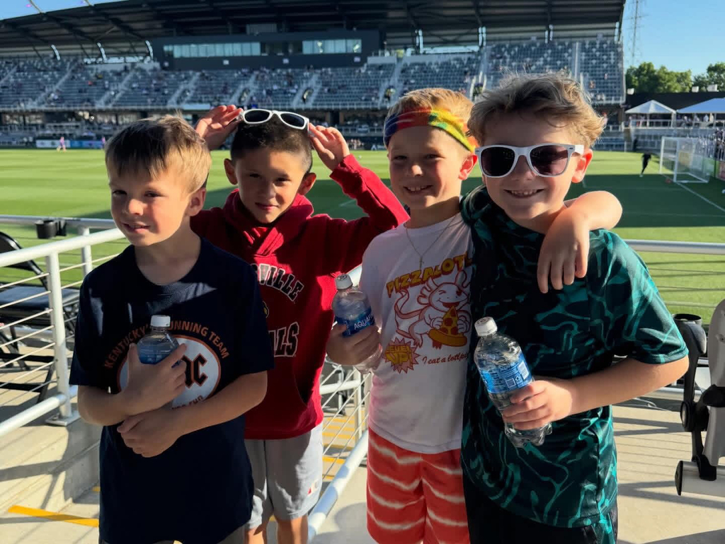 Four boys smiling at the soccer stadium while holding water bottles.