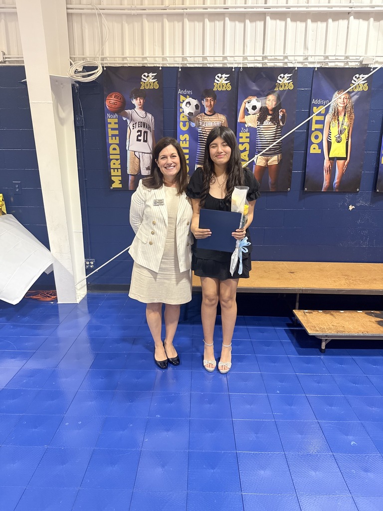 Mercy Academy award recipient smiles with the representative of the school while holding a certificate and flowers.