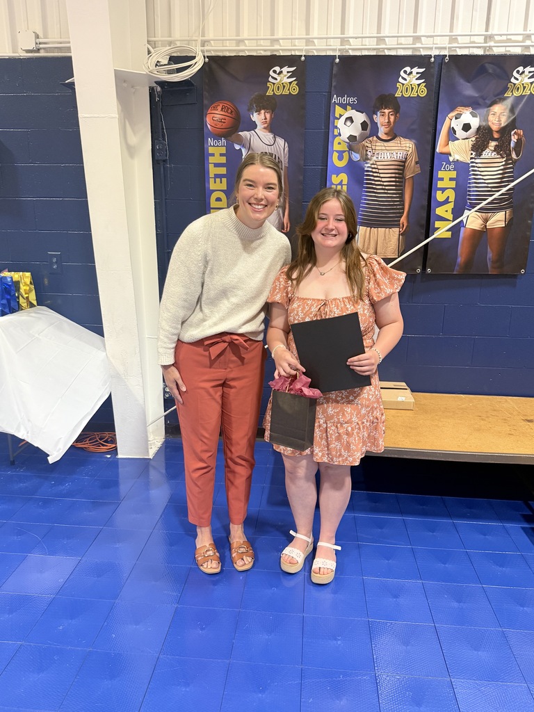 Assumption High School award recipient smiles with the representative of the school while holding a certificate and gift bag.