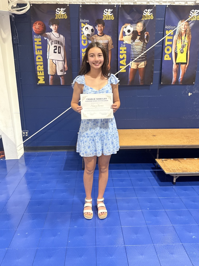 An 8th grade student stands on stage holding the Charlie Shircliff Leadership Award and Scholarship certificate.