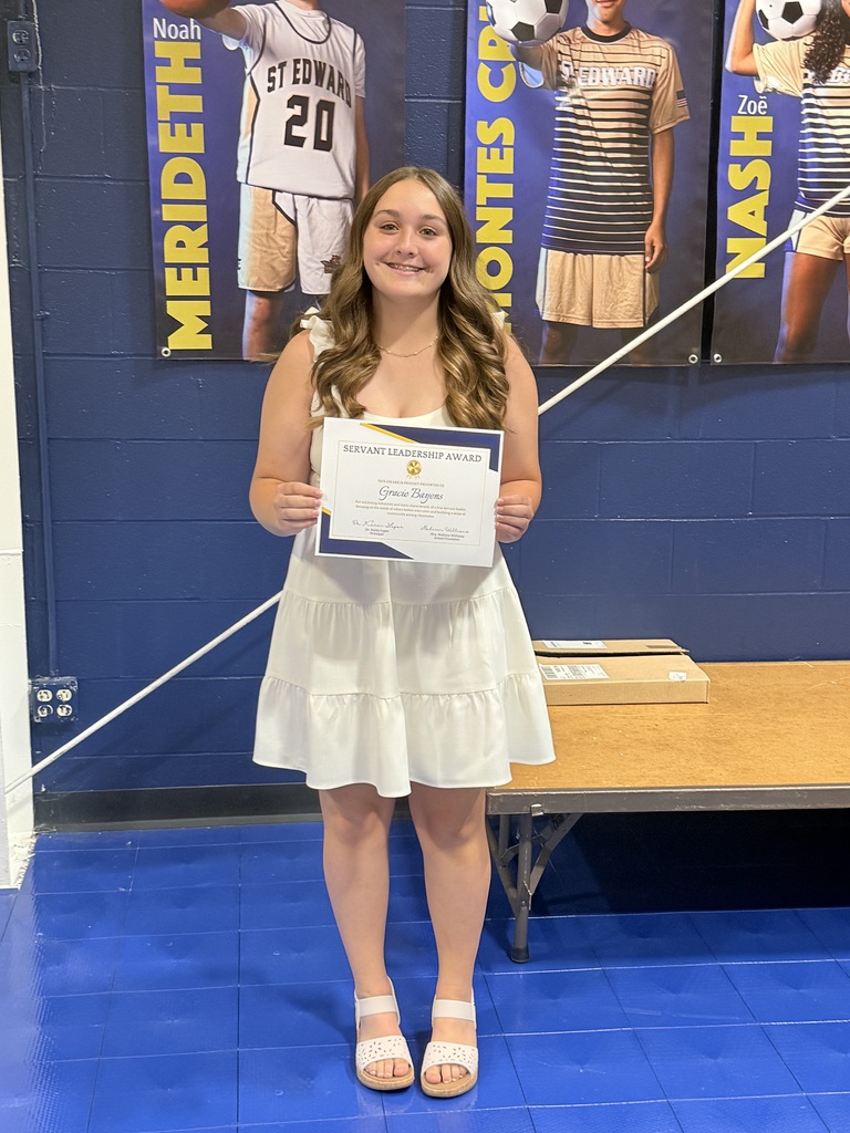 An 8th grade student stands on stage holding a Servant Leadership Award certificate.