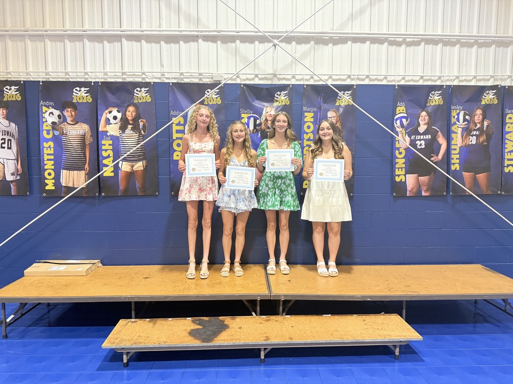 Four St. Edward 8th grade students stand on stage holding award certificates during the Awards Breakfast ceremony.