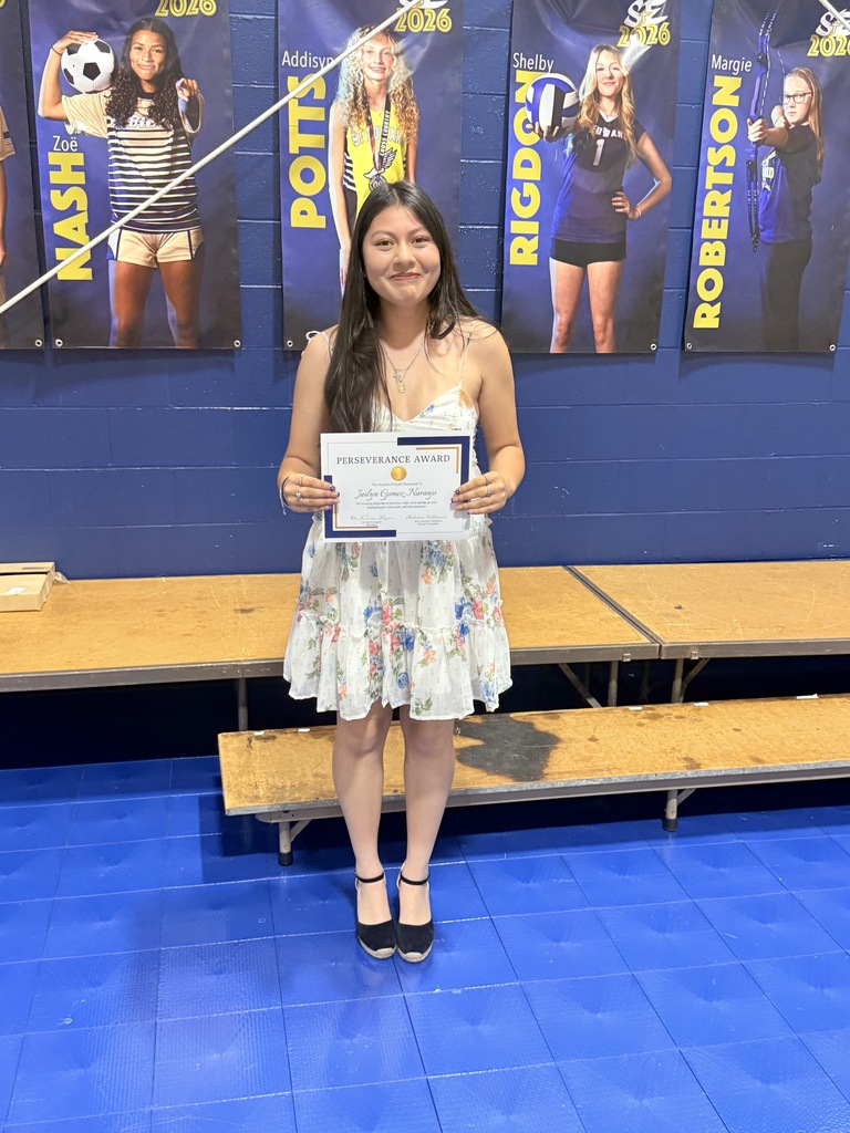 An 8th grade student stands on stage holding a Perseverance Award certificate.