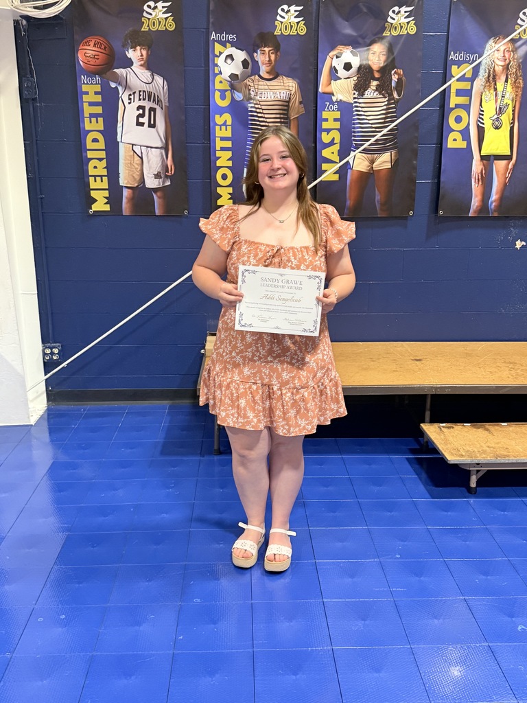 An 8th grade student stands on stage holding the Sandy Grawe Leadership Award certificate.